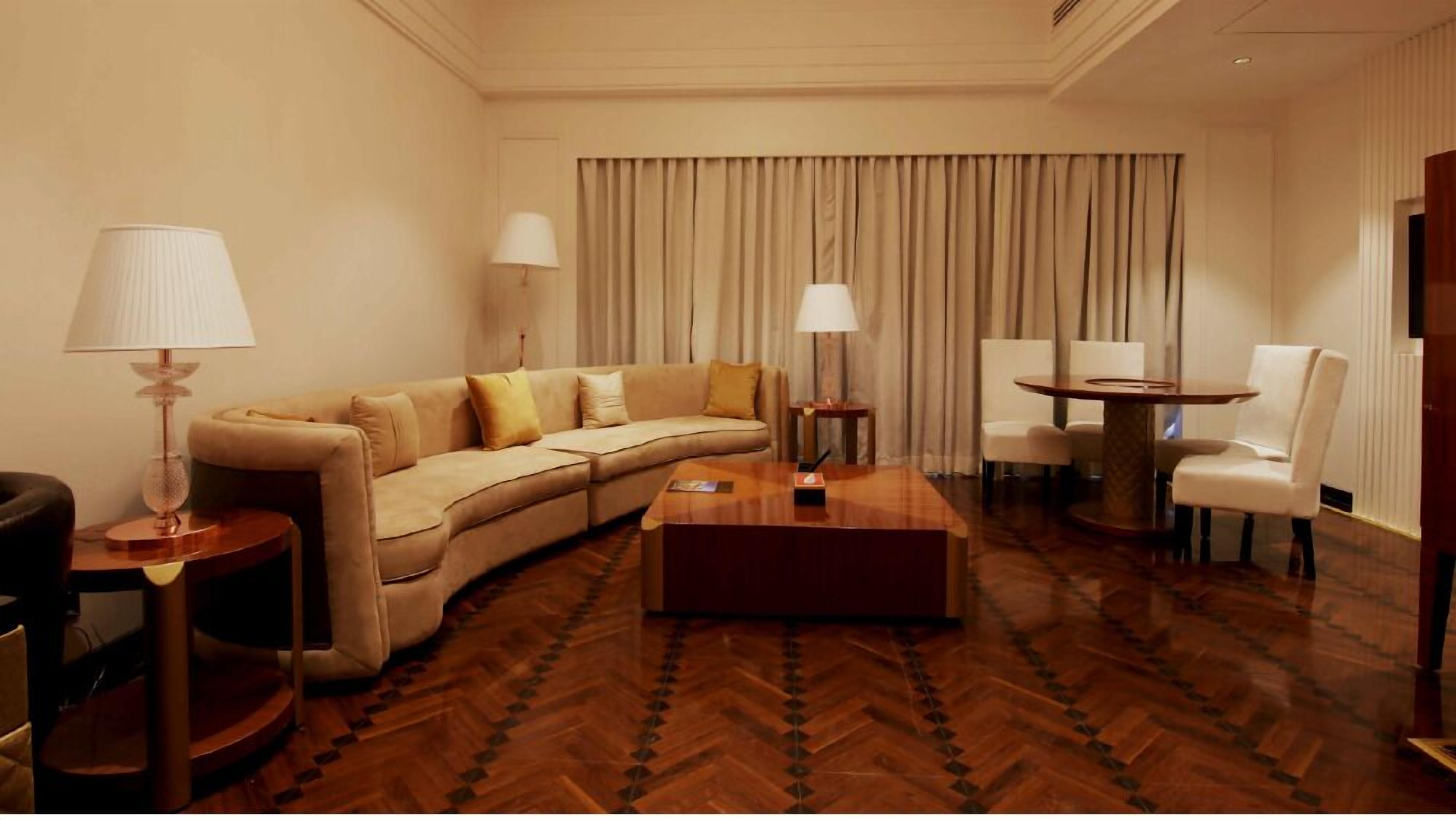 Una habitación de hotel con un sofá curvo, una mesa de centro, una mesa de comedor redonda y dos lámparas.