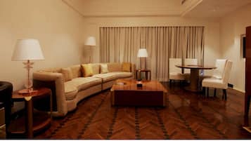 Una habitación de hotel con un sofá curvo, una mesa de centro, una mesa de comedor redonda y dos lámparas.