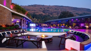 A poolside area with a fire pit, seating, and a view of a hillside. - Della Resorts (Mawal)