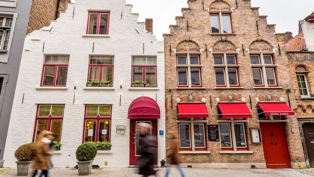 Una hilera de edificios europeos tradicionales con toldos rojos, algunos con señalización que indica un restaurante.