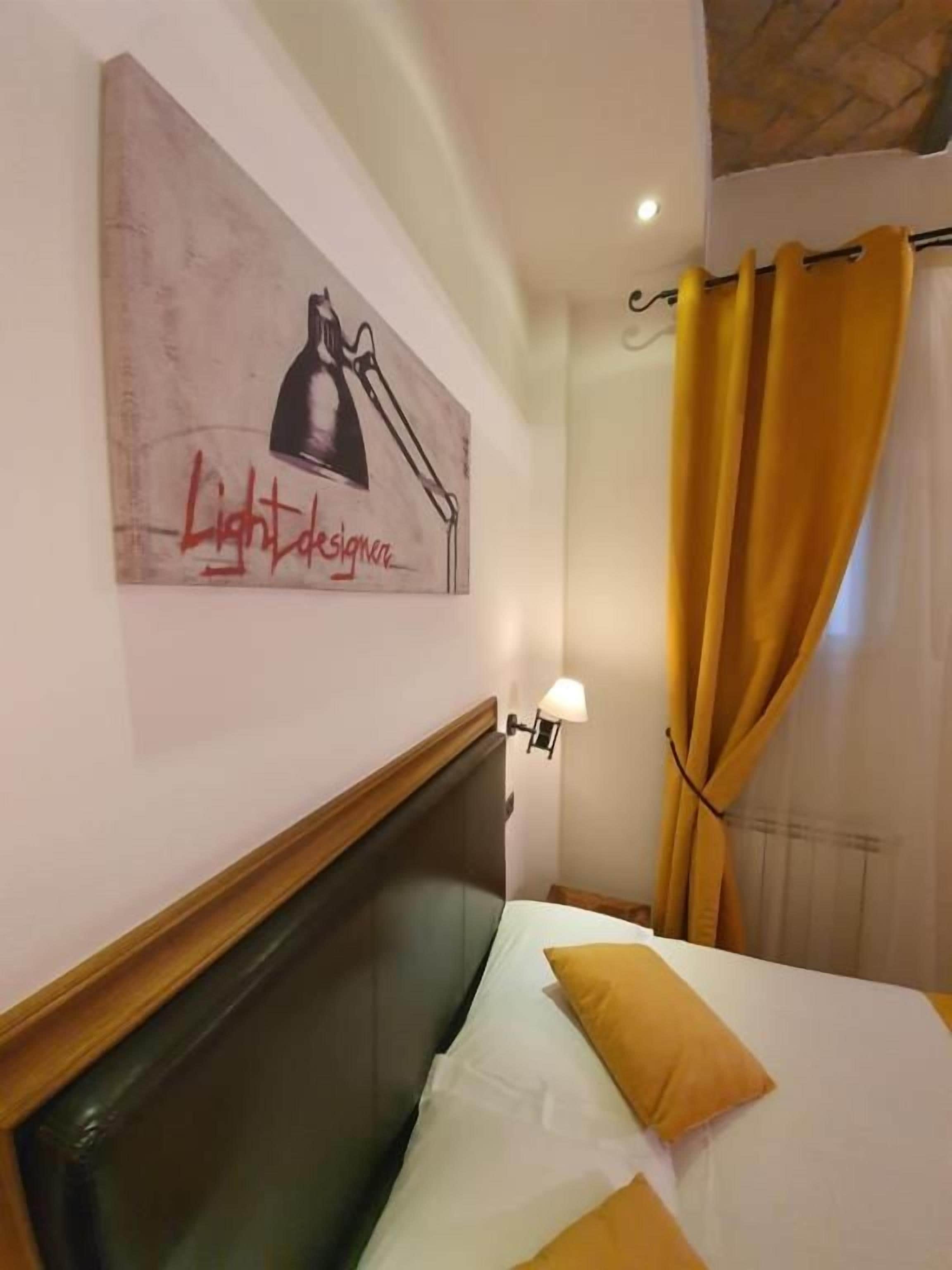 Une chambre d’hôtel avec un lit, une lampe fixée au mur, un tableau et un rideau.