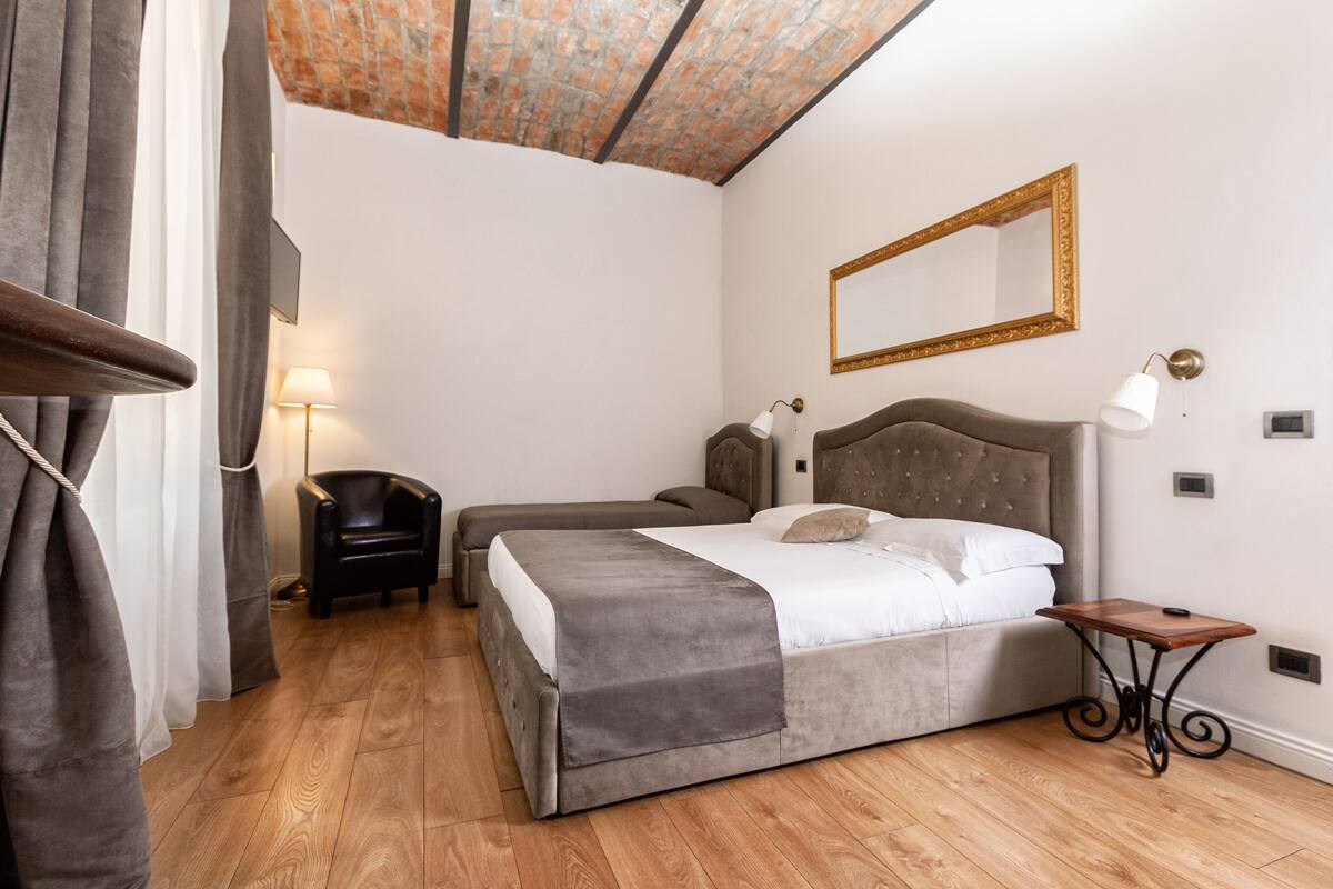 A bedroom with a bed, a chair, a table, a lamp, and a mirror.