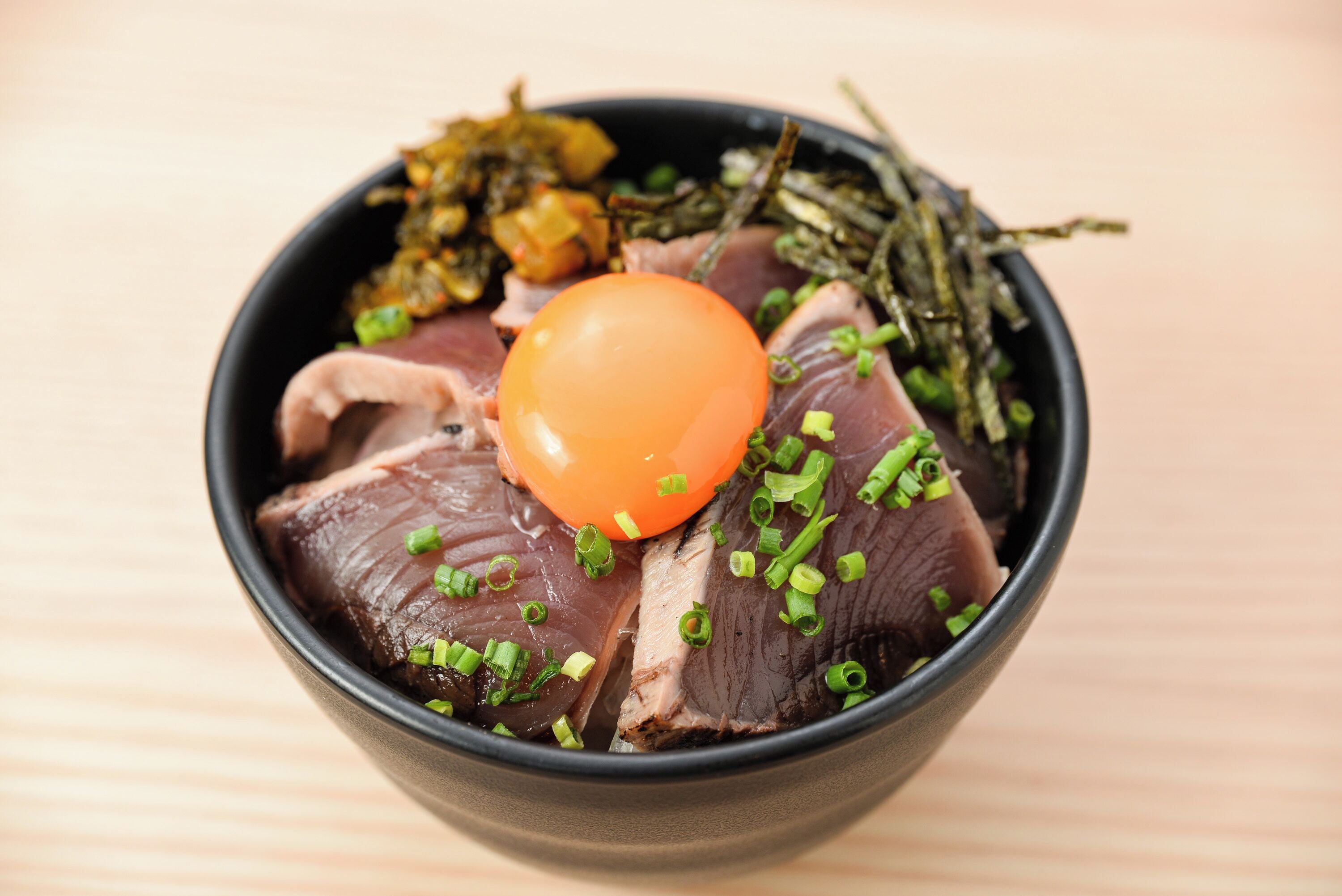 A bowl of sashimi with a cherry tomato and green onions.