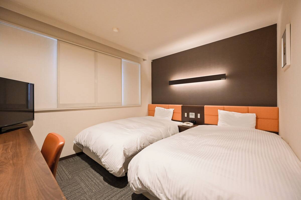 Une chambre d’hôtel avec deux lits, un bureau avec une télévision et un luminaire fixé au mur.