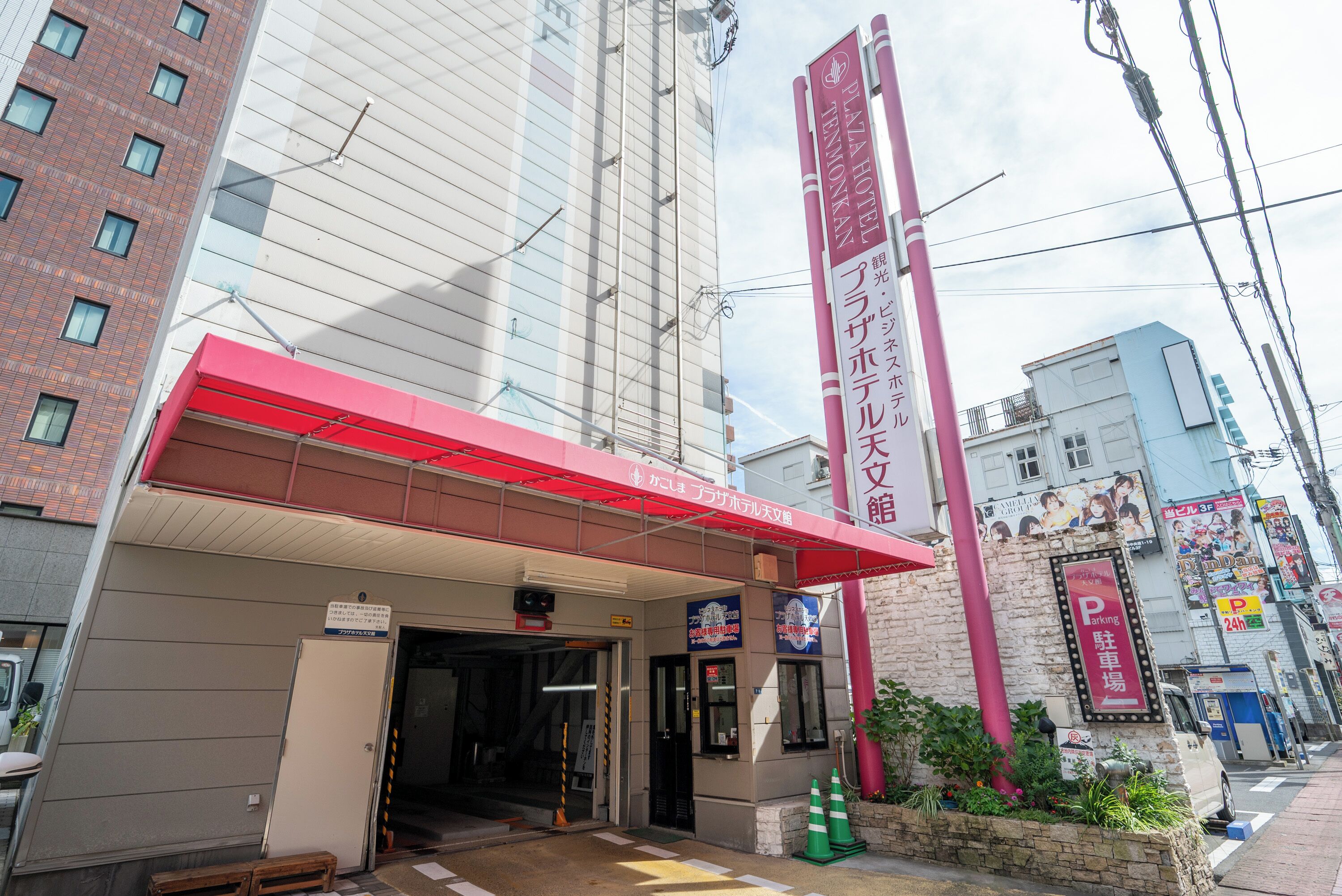 L’entrée d’un hôtel, avec un auvent rouge, une enseigne et un panneau indiquant l’emplacement du parking.