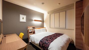A hotel room with a bed, a desk, a chair, a bedside table, a nightstand, a framed picture on the wall, and a window with blinds.