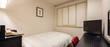 A hotel room with a bed, a desk with a television, a red chair, a telephone, and a framed picture on the wall.