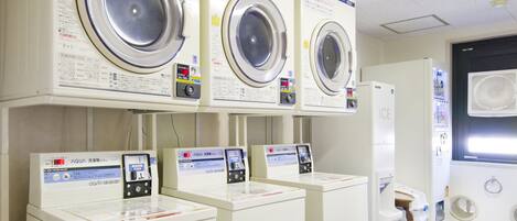 A laundry facility with multiple washing machines and dryers, each with a control panel and instructions.
