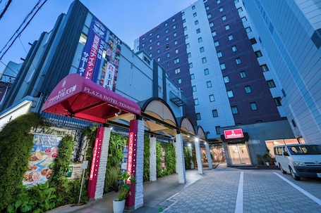 A hotel entrance with a red awning, a signboard, and a modern building in the background.