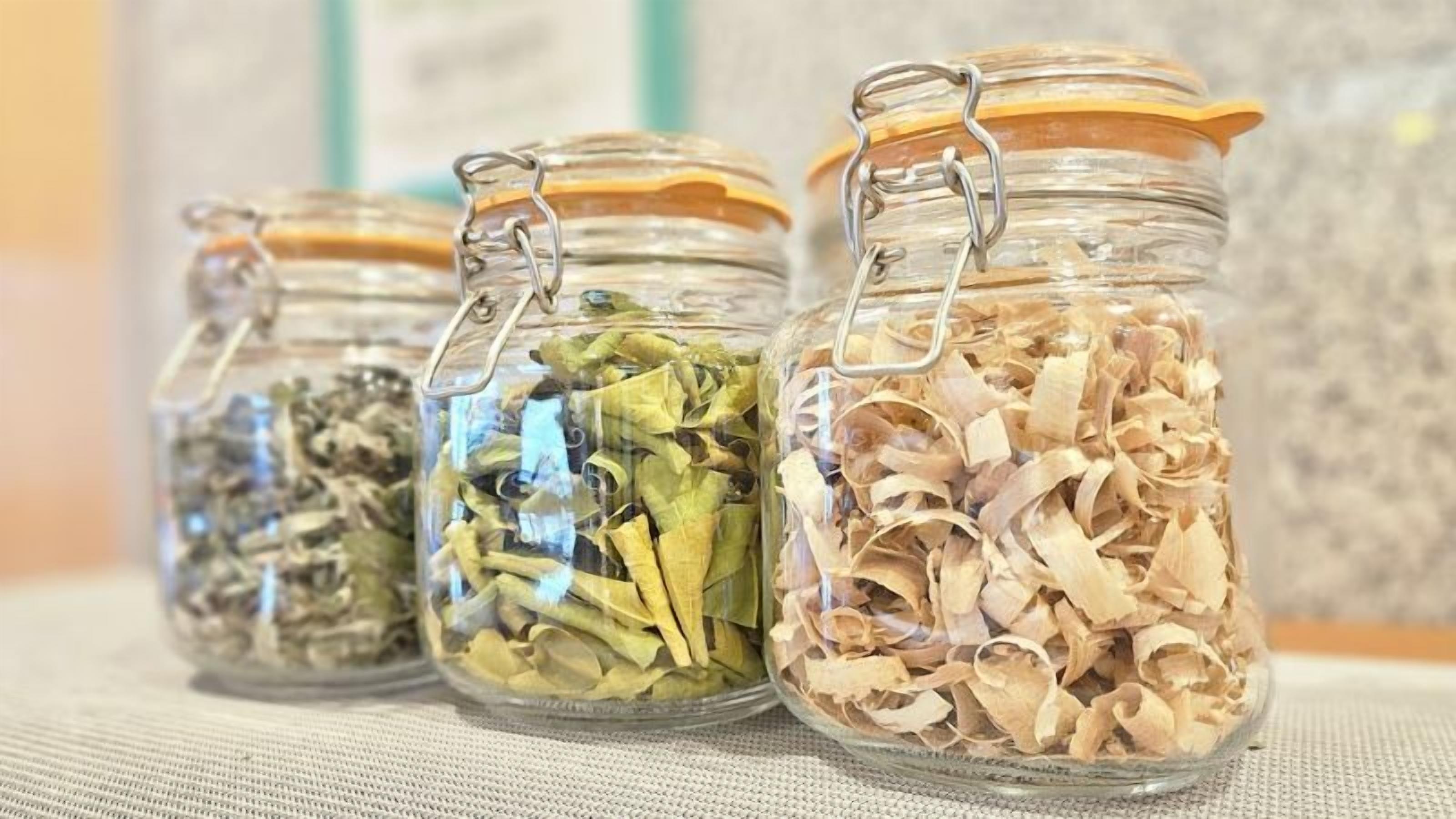 Four glass jars with metal clasps, containing dried leaves and herbs.