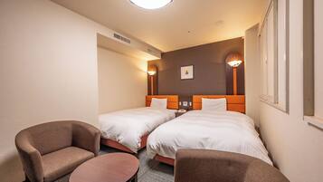Habitación de hotel con dos camas individuales, una mesita redonda pequeña, dos sillones y una lámpara de pared.