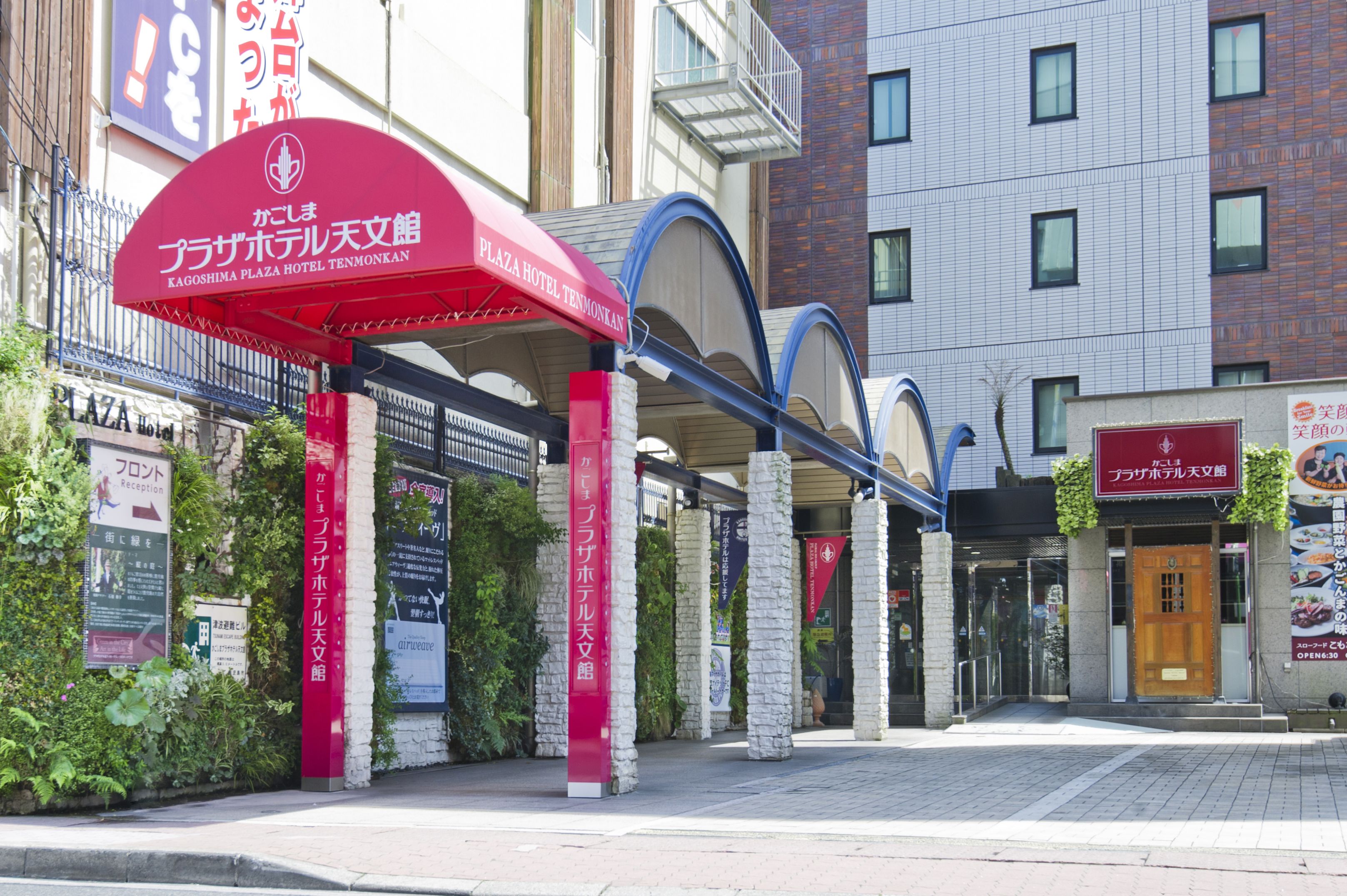 La entrada del Hotel Kagoshima Plaza Tenmonkan, con un toldo rojo y pilares de piedra.