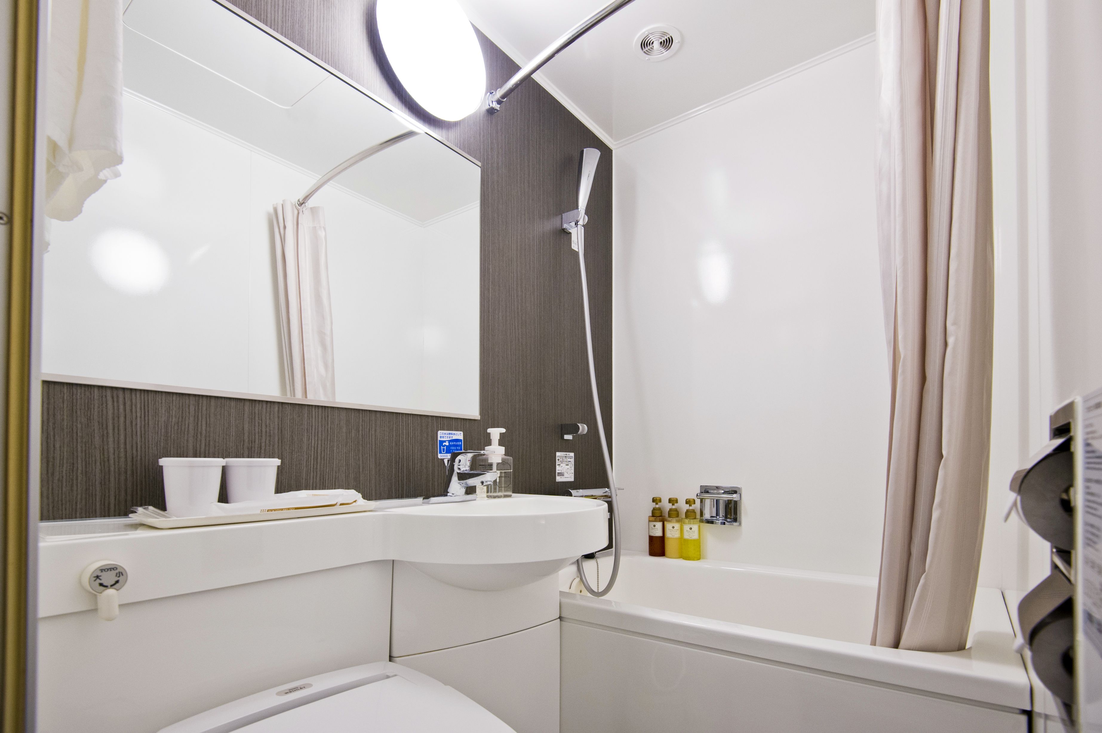 A modern bathroom with a white sink, mirror, and shower. There are toiletries on the wall and a towel rack.
