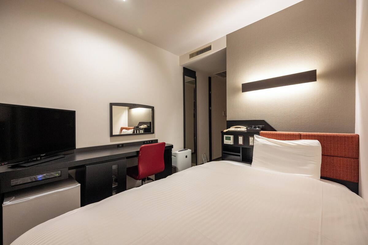 Une chambre d’hôtel avec un lit, un bureau, une télévision, une chaise rouge et un téléphone.