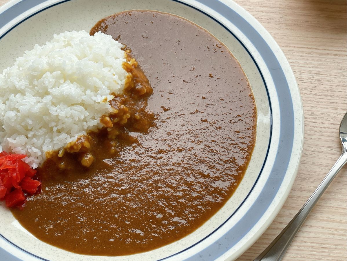 A plate with white rice and a brown sauce, possibly curry, on a table.
