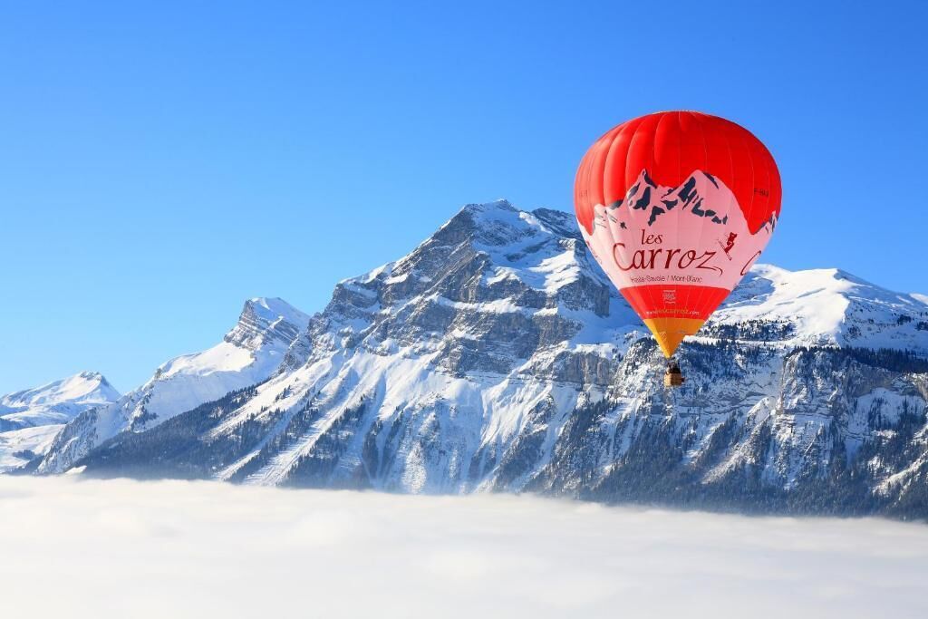 A hot air balloon with "les Carroz" text over a snowy mountain range.