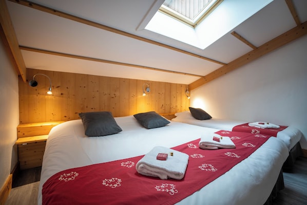 Un dormitorio con tragaluz, vigas de madera, una cama grande con almohadas y una colcha roja decorativa.
