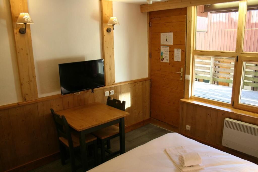A wooden-paneled room with a bed, a table, chairs, a television, and a window with blinds.