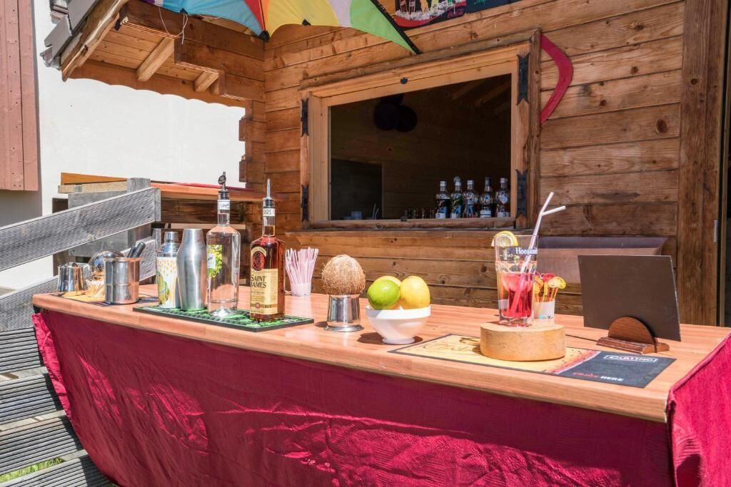 Zona de bar con barra de madera, mantel rojo, botellas de whisky Saint James, un frutero y un atril para el menú.