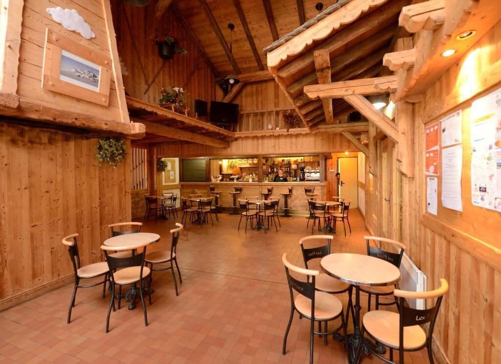 A wooden interior with multiple tables and chairs, a bar area, and a view of the outside.