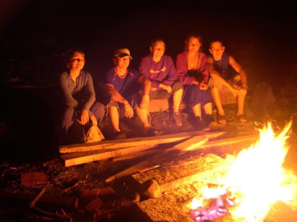 A group of people sitting around a campfire at night.
