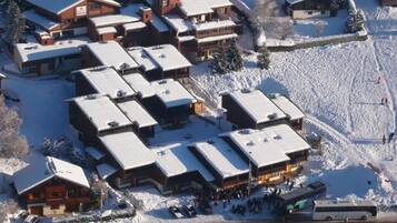 Un complejo turístico cubierto de nieve con varias construcciones de estilo chalet, un área de estacionamiento y un autobús.