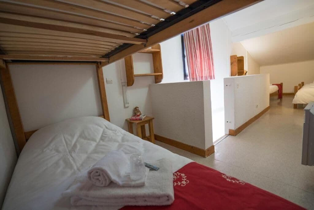 Una habitación pequeña y funcional con una cama litera, una mesita con un adorno y una kitchenette.