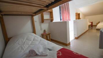 Una habitación pequeña y funcional con una cama litera, una mesita con un adorno y una kitchenette.