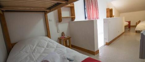 A small, compact room with a bunk bed, a small table with a decorative item, and a kitchenette area.