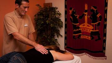 A massage therapy session in a room with a large plant and a tapestry depicting African figures.