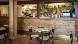 Zona de bar con paredes de madera, una barra con diferentes botellas y varias mesas y sillas.