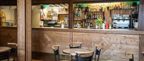 Zona de bar con paredes de madera, una barra con diferentes botellas y varias mesas y sillas.