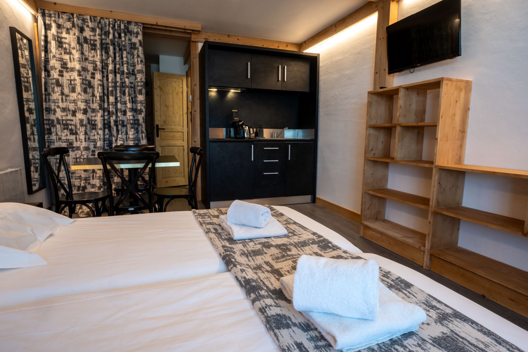 Una camera d'albergo con un letto, una scrivania, una sedia, angolo cottura e televisione.