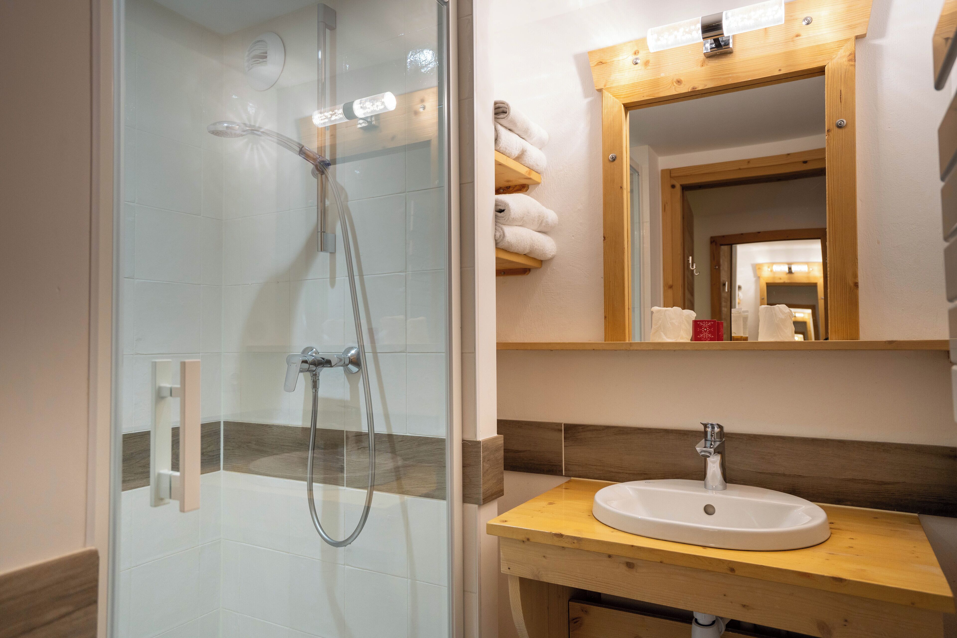 A bathroom with a glass-enclosed shower, a wooden vanity with a sink, and a mirror above the vanity.