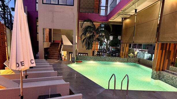 Zona de piscina con escalones que conducen a un deck cubierto, rodeada de arquitectura moderna y mobiliario exterior.