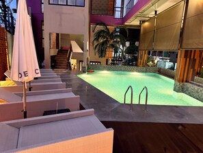 A swimming pool area with steps leading to a covered deck, surrounded by modern architecture and outdoor seating. - De coze' Hotel (Patong)