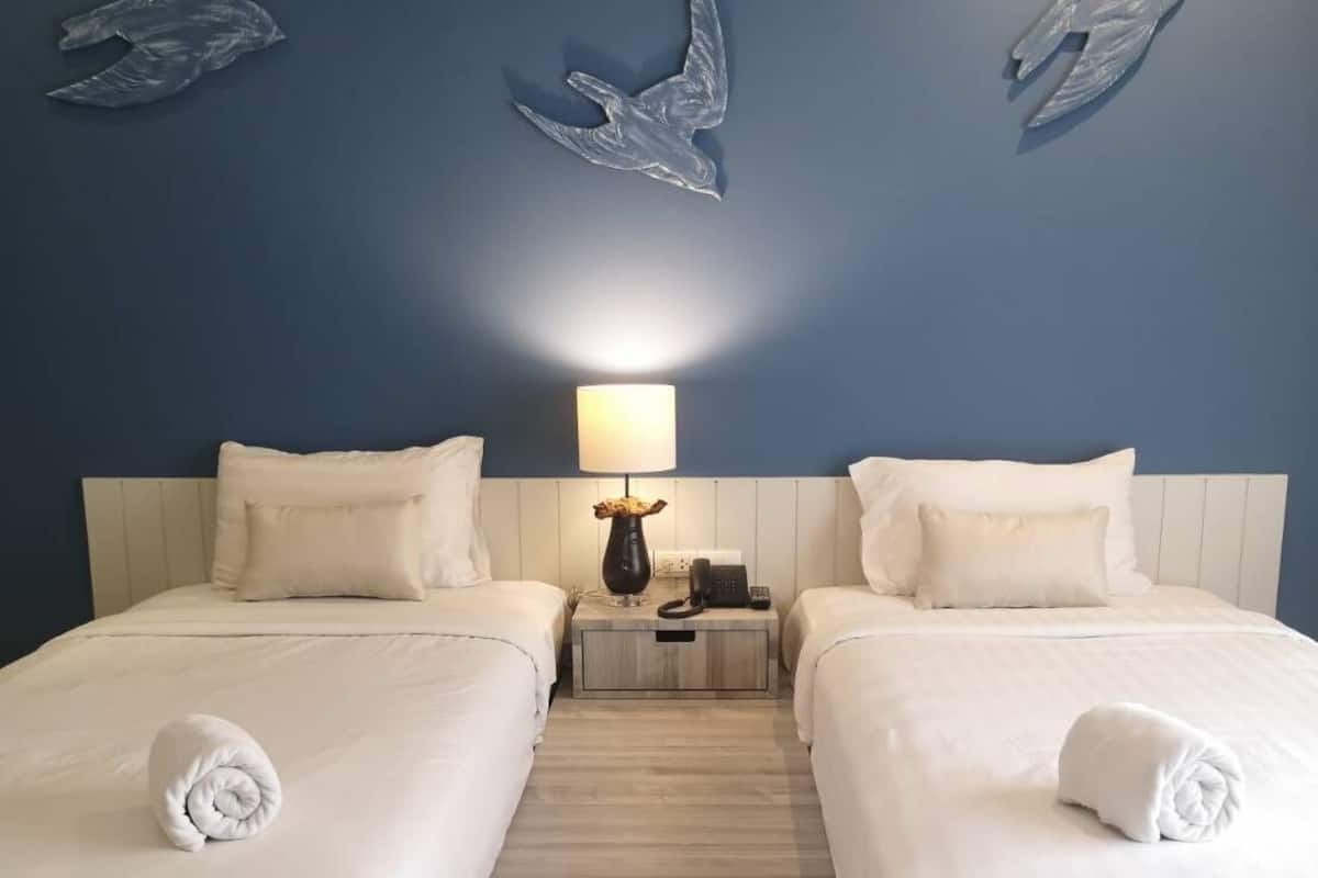 A hotel room with two beds, a nightstand, a lamp, and wall art of birds.