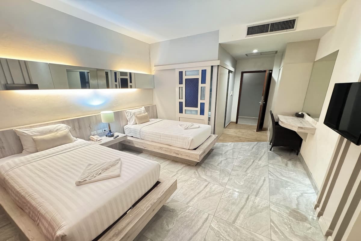 A hotel room with two beds, a desk, a TV, and a bathroom.