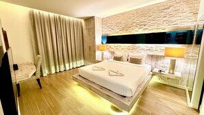 Una habitación de hotel moderna con una cama grande, un cabecero de madera, un televisor de pantalla plana y una mesita de noche con lámpara.