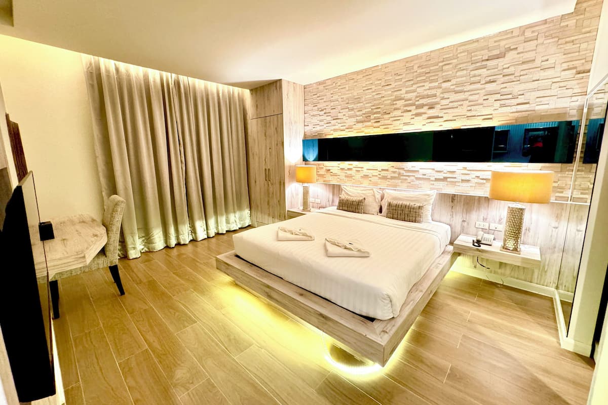 A modern hotel room with a large bed, a wooden headboard, a flat-screen TV, and a nightstand with a lamp.