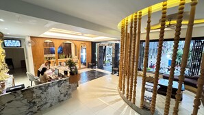 Un vestíbulo de hotel con una recepción de mármol, detalles de madera y vistas a la calle a través de amplios ventanales.