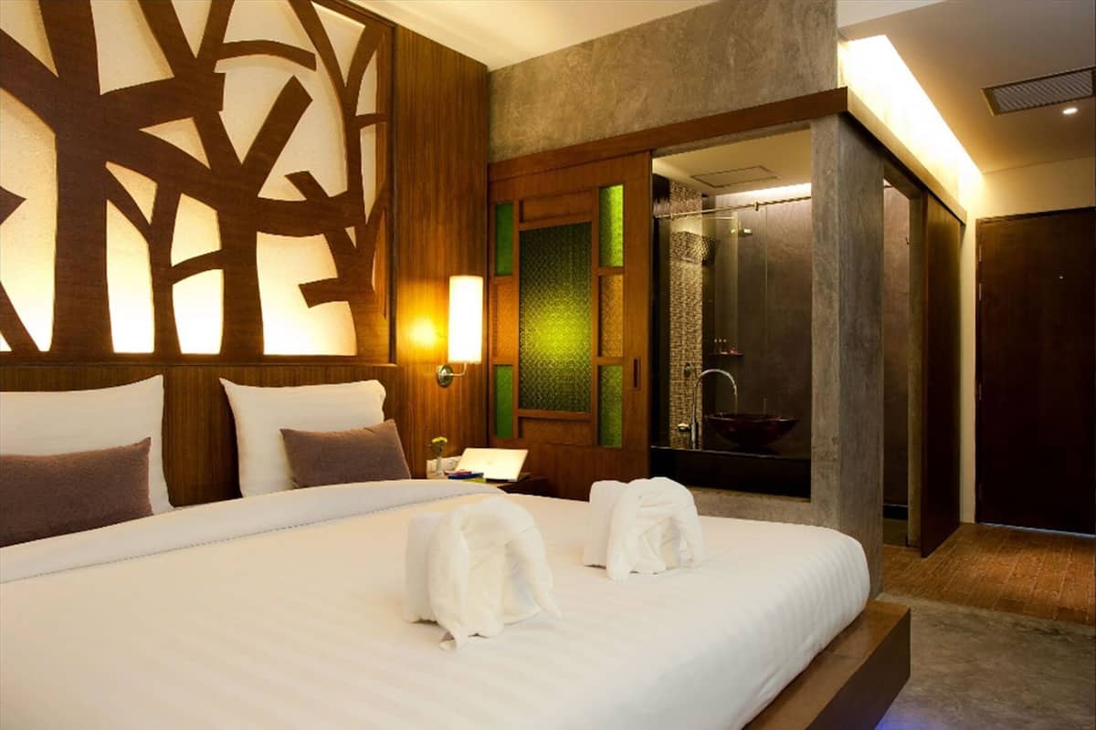 A hotel room with a large bed, a bathroom with a glass-enclosed shower, and a wooden wall design.