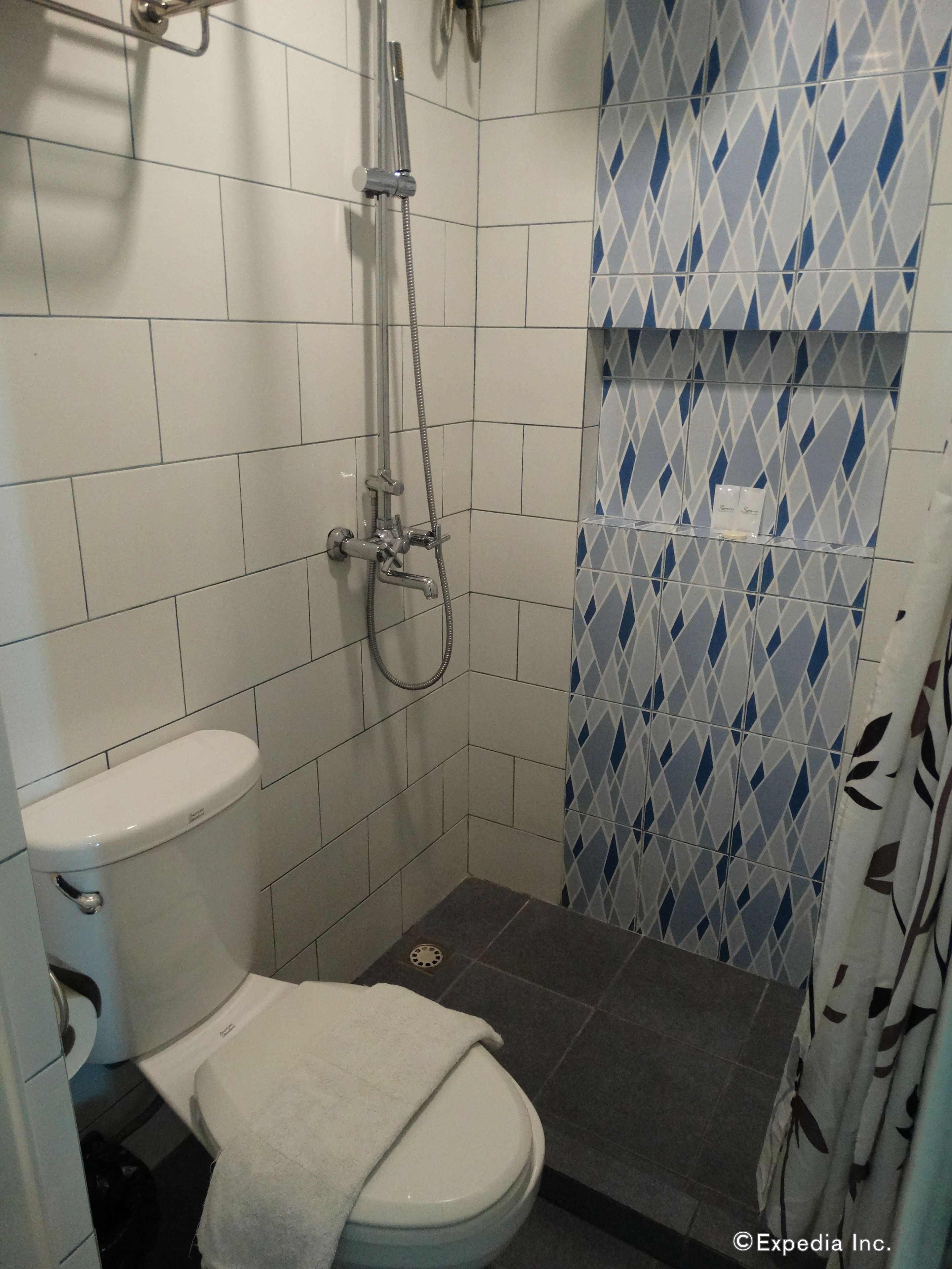 A small, tiled bathroom with a toilet, shower, and a patterned wall.