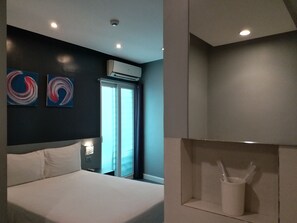 A modern hotel room with a large bed, two abstract wall art pieces, an air conditioning unit, a window with curtains, and a small white cabinet with a spoon and cup. - Leez Inn Malate (Manila)