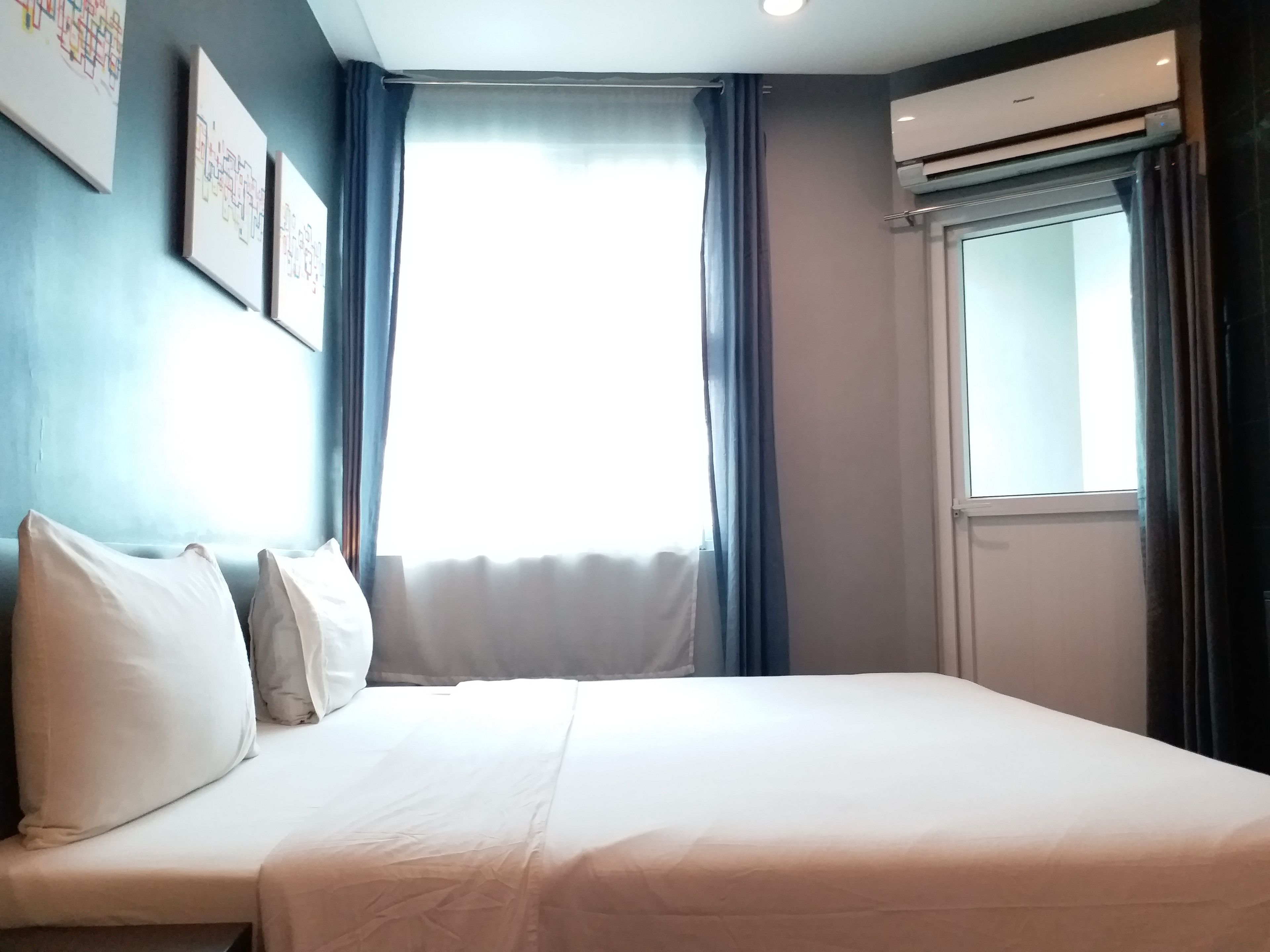 Una habitación de hotel con una cama, una ventana con cortinas y un equipo de aire acondicionado.