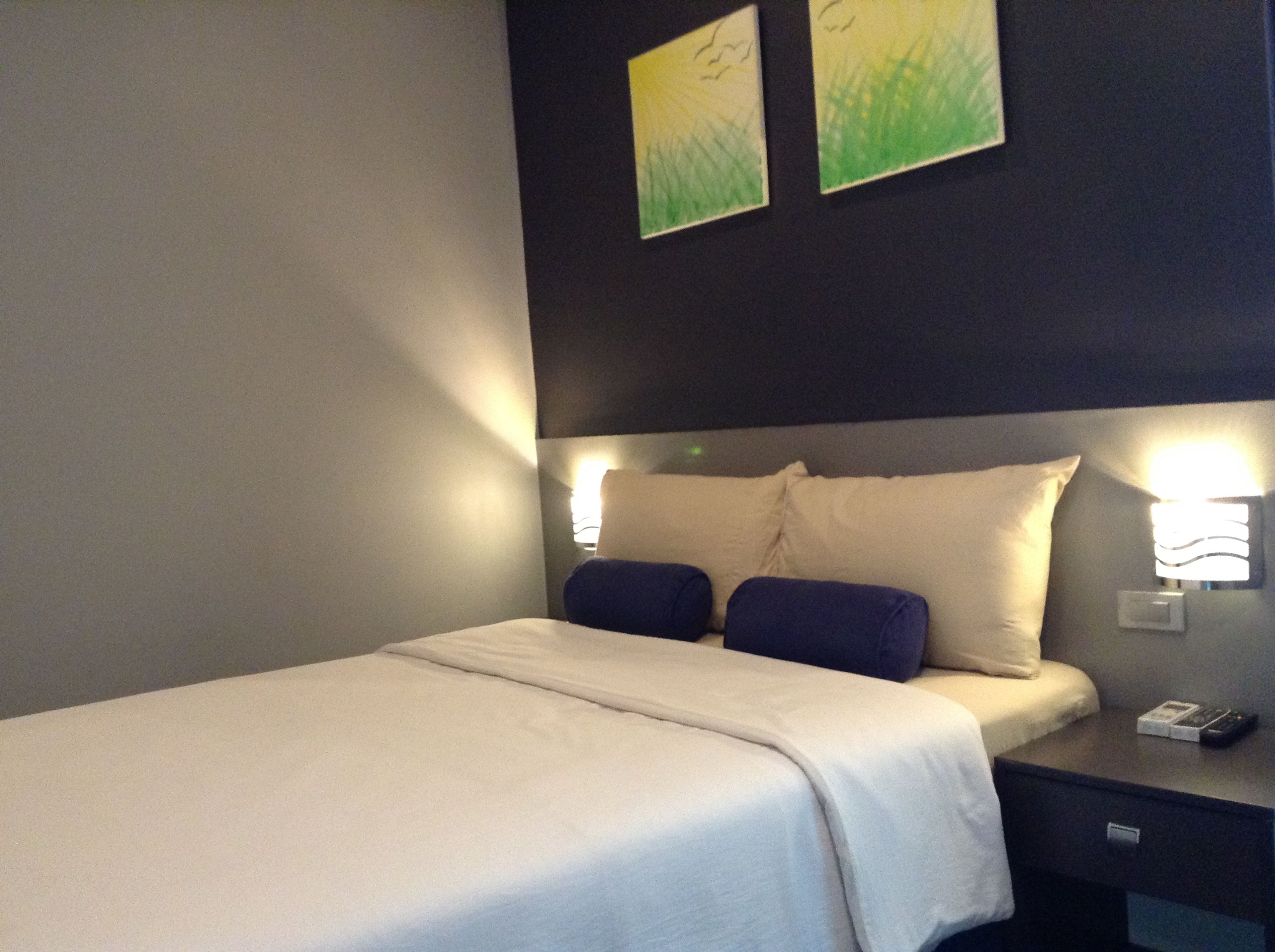 Una habitación de hotel con una cama, una mesita de noche y dos lámparas fijadas a la pared.