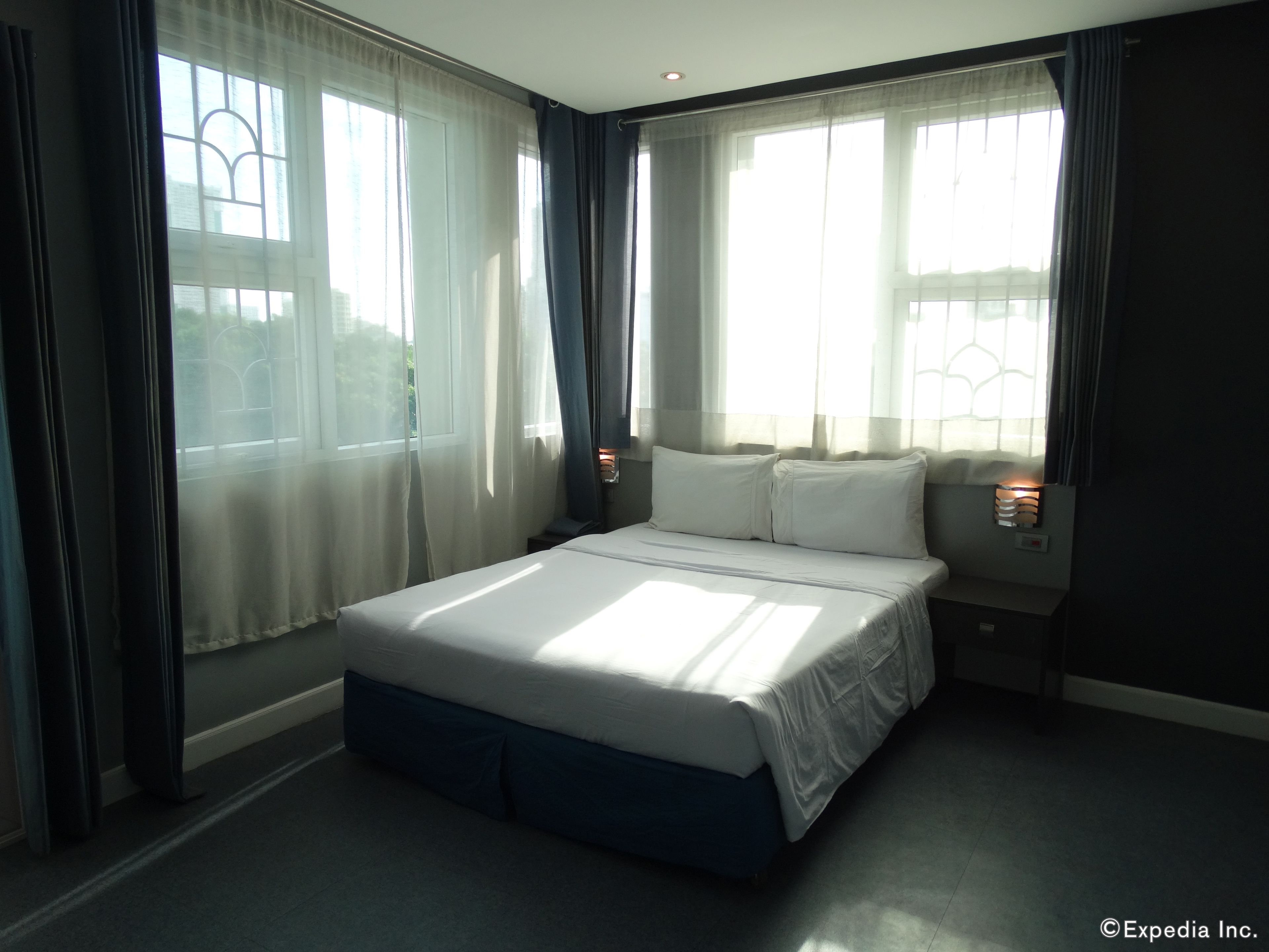A hotel room with a large bed, a nightstand, and a window with curtains.