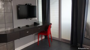 A modern hotel room with a dark grey desk, a red chair, a flat-screen TV, and a large window with curtains. - Leez Inn Malate (Manila)