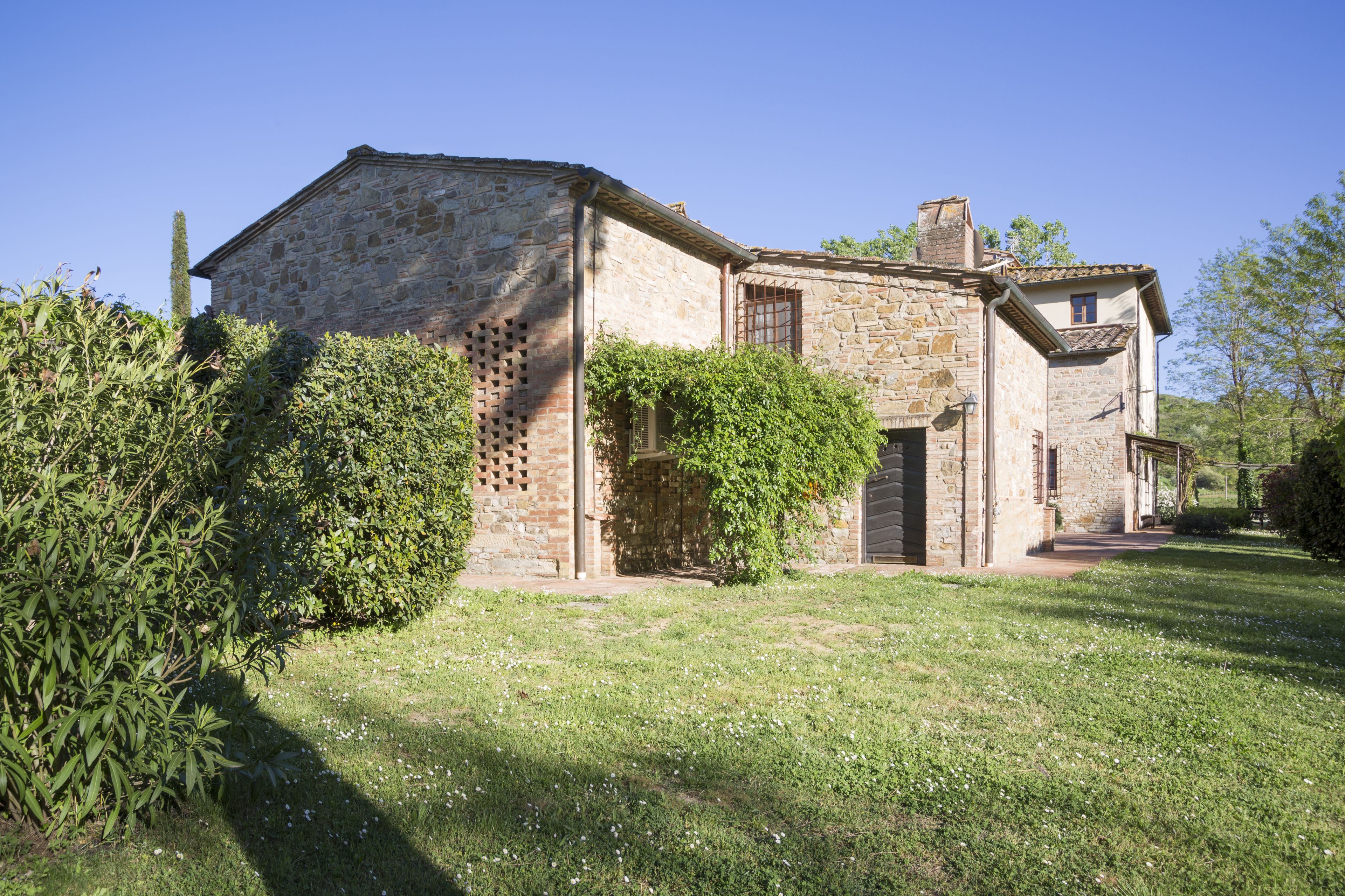 A stone building with a traditional design, featuring a covered porch and a small garden area with grass and bushes.