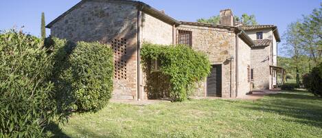 A stone building with a traditional design, featuring a covered porch and a small garden area with grass and bushes.
